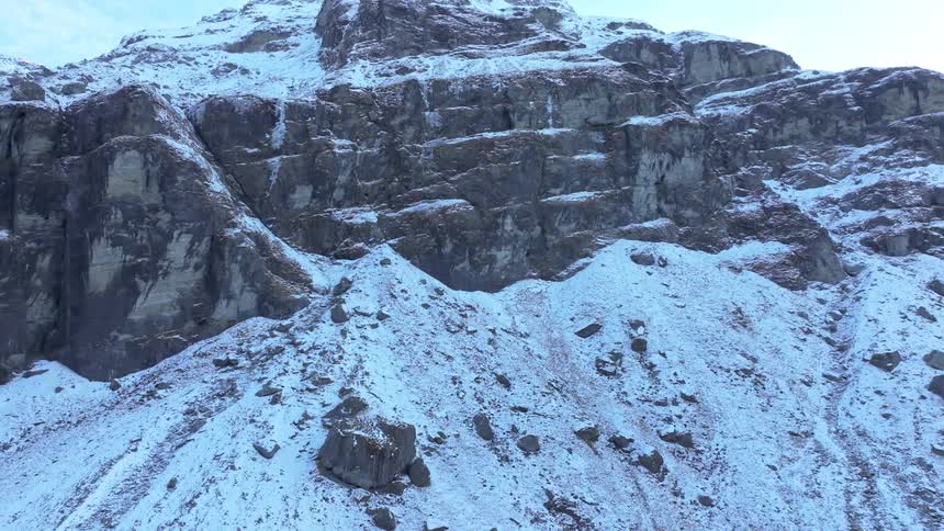 A steep rocky mountain slope covered in patches of snow and scattered rocks dominates the frame extending upwards towards a bright sky