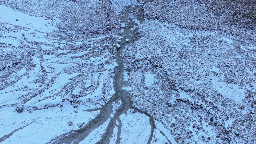Aerial view of snowy mountain valley with narrow stream