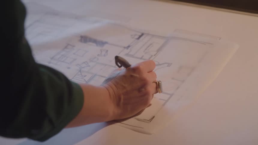 A man uses a pen to write on an architectural building plan laid out on paper