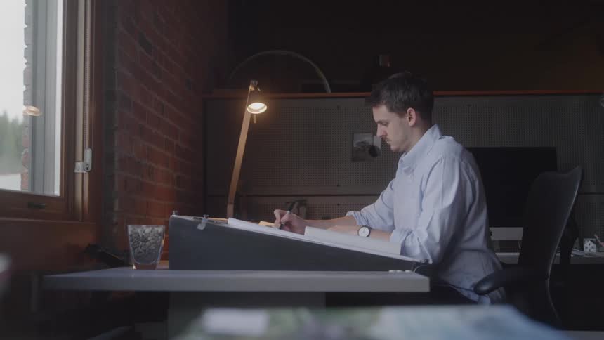 The architect is working in his office writing on a blueprint