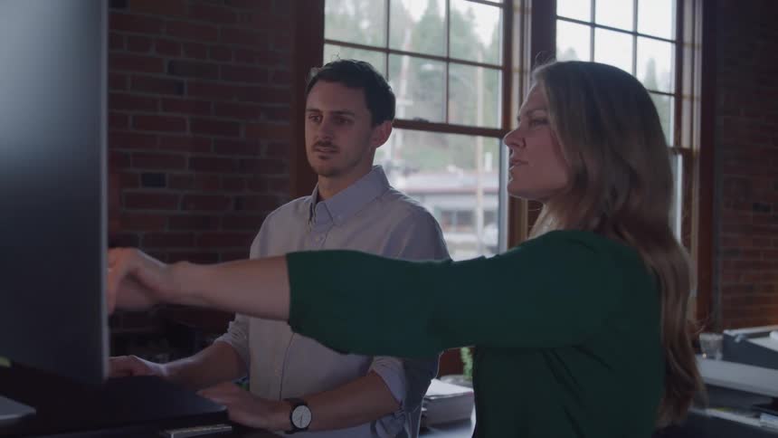 Two workers in the office use a computer together