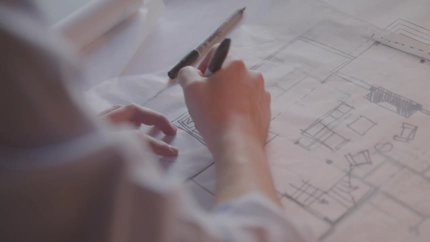 An architect uses a pen to draw a building plan on a white cardboard sheet