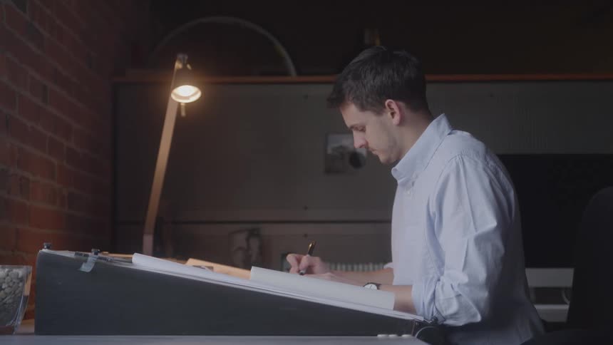 A man stands at a drafting desk while making notes on a schematic