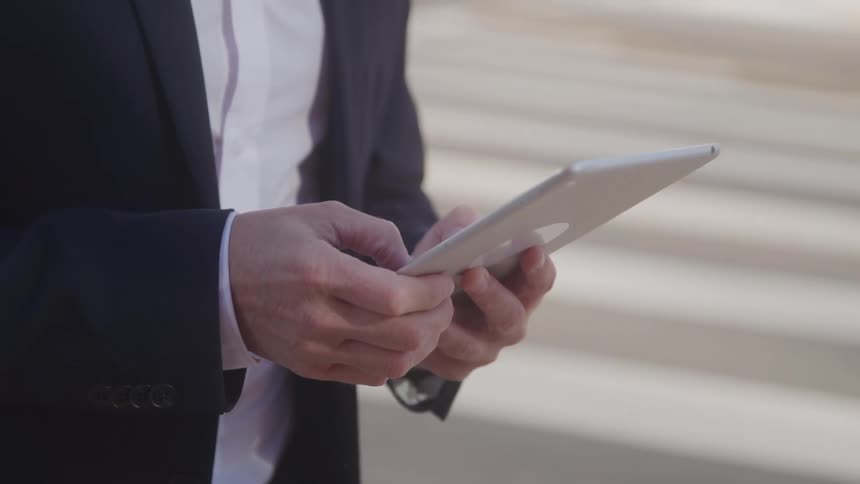 The man is typing on his tablet outside