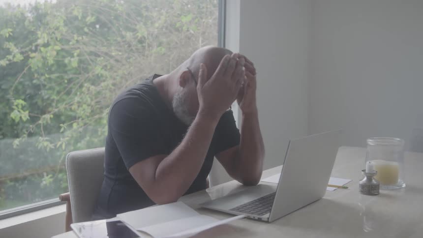 The man is thinking while sitting by his laptop