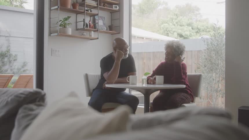 An elderly black couple discuss while sitting at a table in a living room during daytime