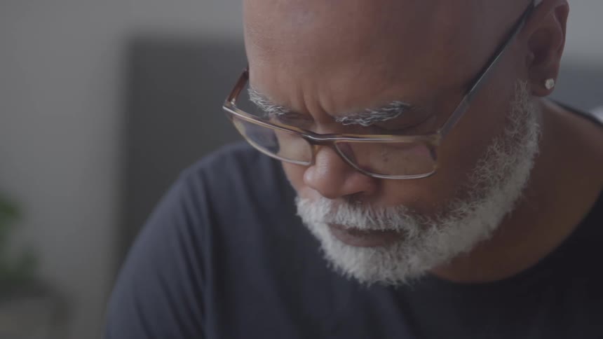 An older man concentrates on something while frowning