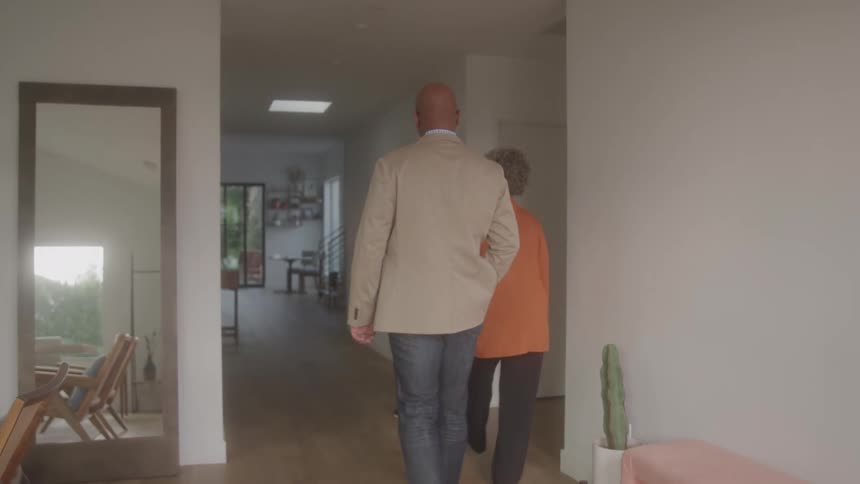 A woman gestures down a hallway while showing a welllit modern home to a smiling black couple