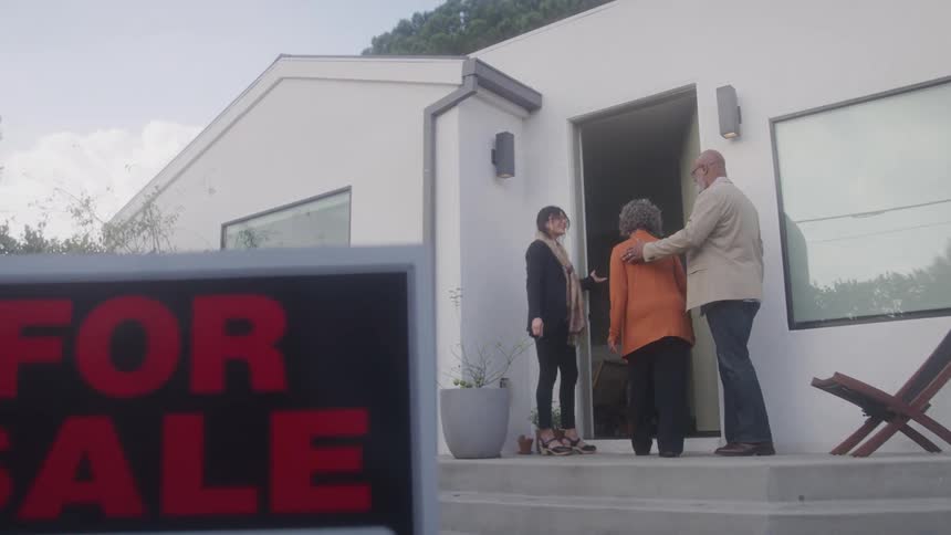 A female realtor opens the door to a house for a couple to enter