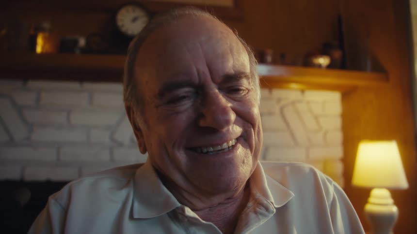 Elderly man sitting in a wheelchair near the fireplace in his living room enjoys looking at his smartphone