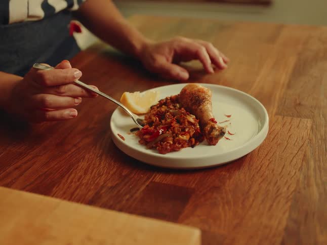 This video offers a closeup of a persons hands skillfully using a fork to separate and lift a piece of chicken and what appears to be paella or a similar rice dish from a white plate the setting is a warm wooden table emphasizing the culinary experie