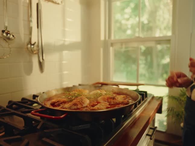 Woman adds garnish to the chicken cooking in sauce on the stove