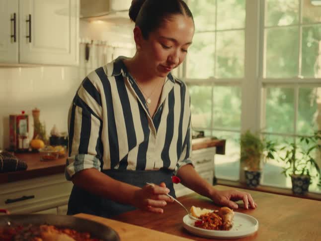 Woman smiles while tasting a chicken dish at the island in her kitchen during the daytime