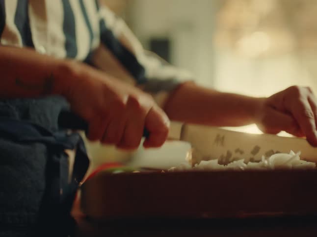 Pair of hands with a knife chopping onion on a wooden cutting board
