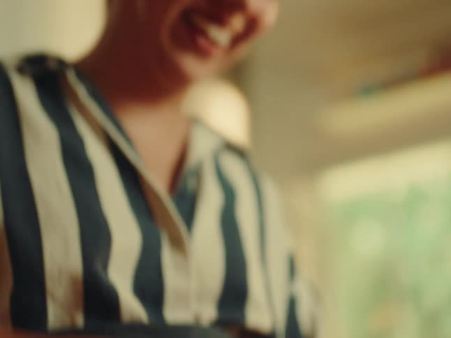 A woman in a striped shirt initially seen meticulously chopping an onion on a cutting board then looking down with a bright happy smile suggesting satisfaction with her cooking