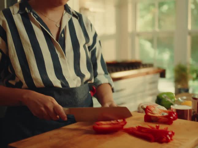 Woman with a knife cutting a red bell pepper on a wooden cutting board