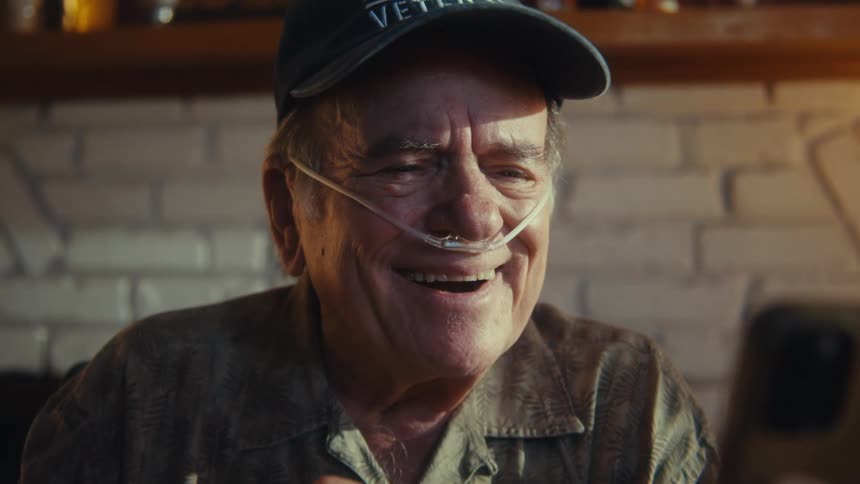 Oxygen tube in the nose of an elderly man in a cap with a happy expression interacting with a smartphone