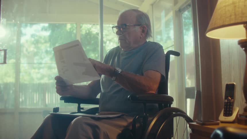 Elderly man in a wheelchair reading a document