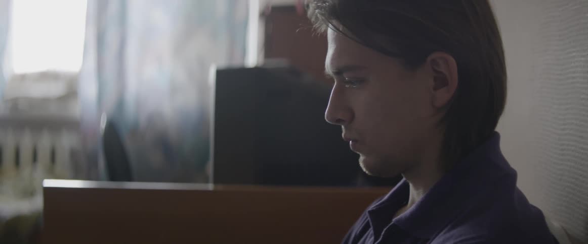 Man with brown hair sits near a computer
