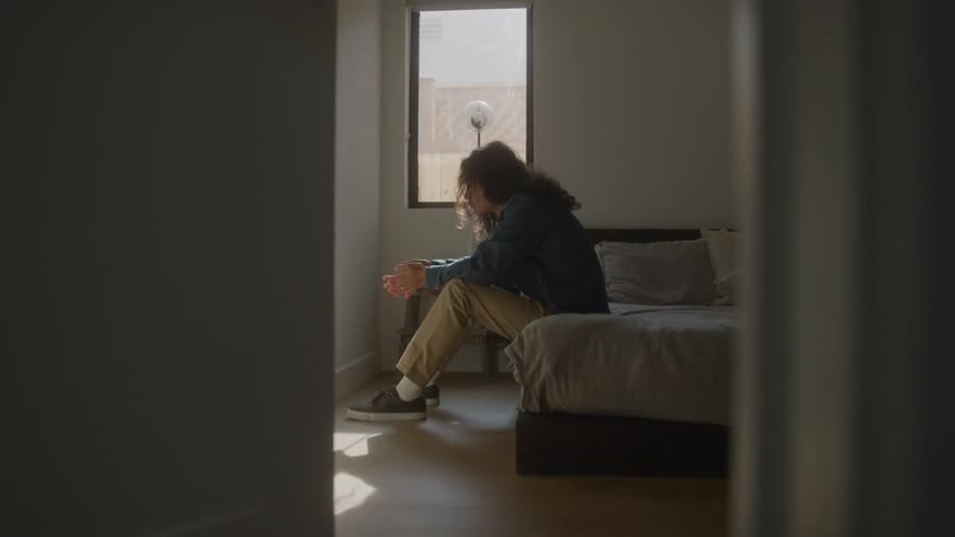 Person sits on bed edge looking sad
