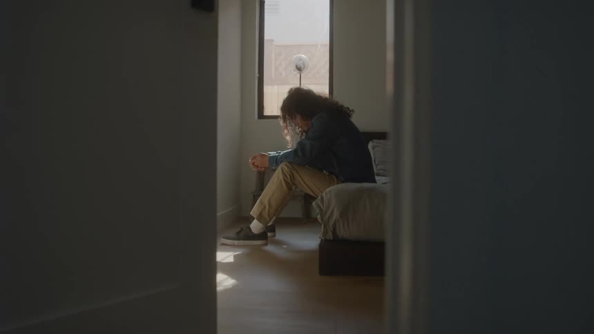 Man sitting on bed with his head down