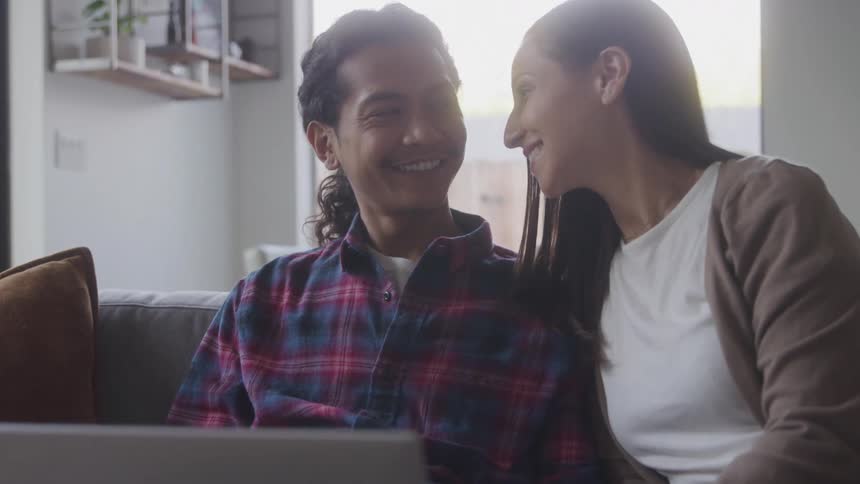 Couple sits closely on a couch having a conversation while looking at a laptop