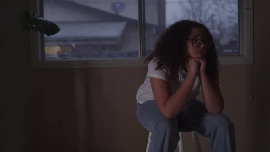 Woman with glasses and curly hair sitting with her hands on her chin