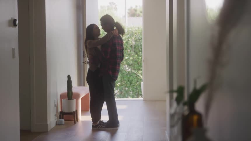 A man and a woman are embracing in the hallway of a whitewalled house and are moving romantically