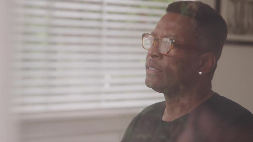 A man wearing glasses earrings and a black tshirt is indoors