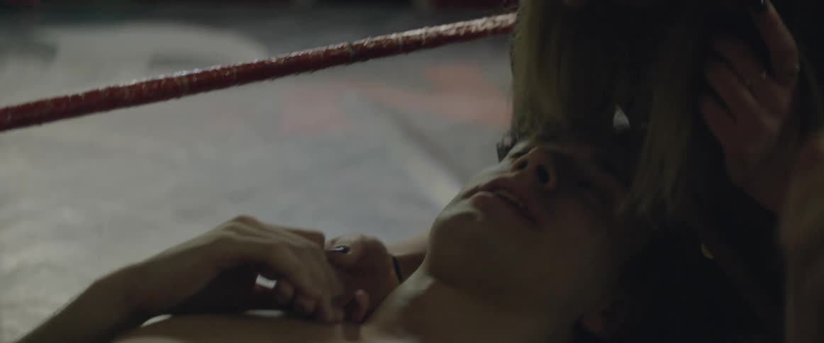 A woman leans down and kisses a man as they rest outside a fight ring