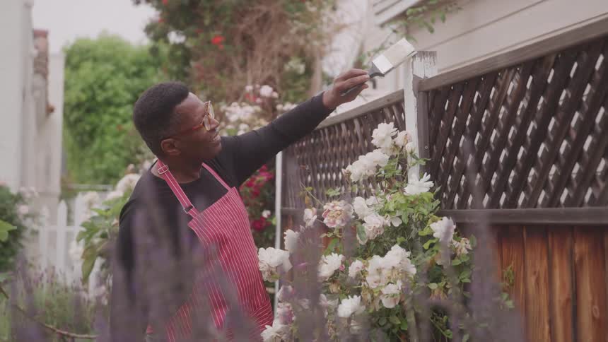 Man painting a wooden flowerbed with white paint