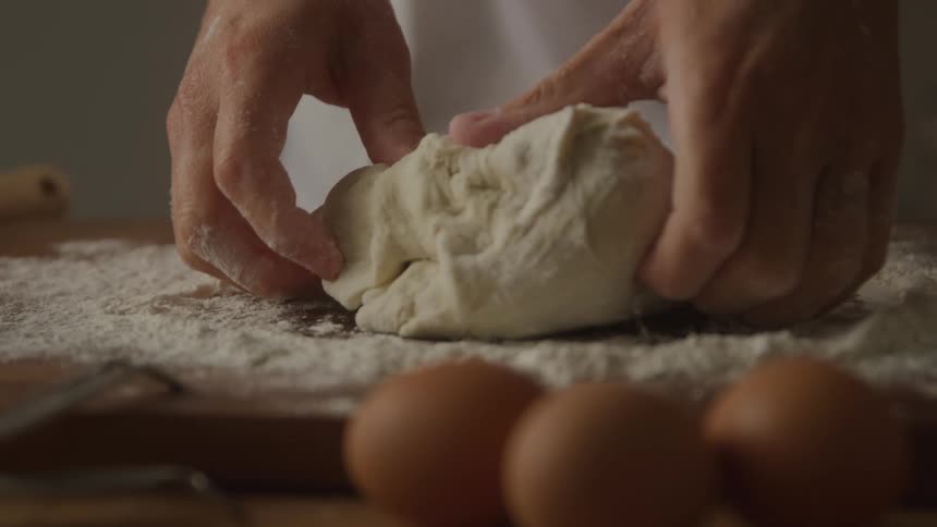 A person molds dough while sprinkling flour to smooth it with three eggs placed on the side