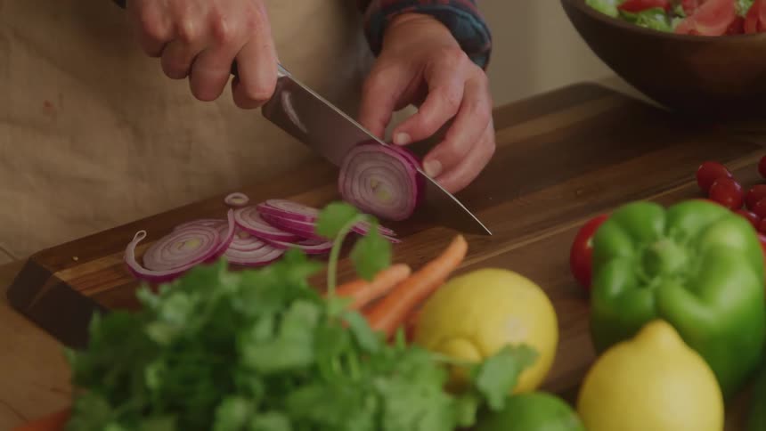 Person with a knife slicing red onion strips on a cutting board