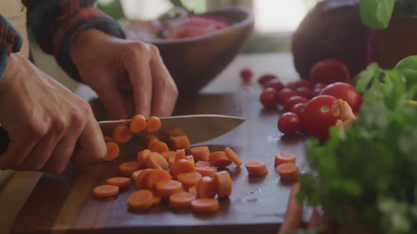 A person cuts carrots on a chopping board with vegetables and tomatoes on the side