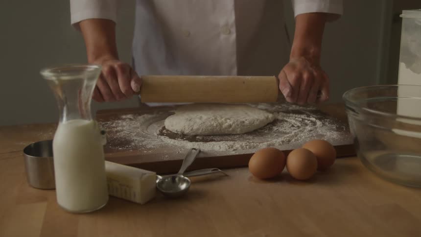 Chef with a wooden rolling pin kneading a dough sprinkled in wheat on a table