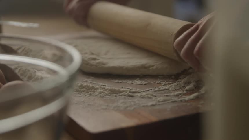 Person with a wooden rolling pin kneading dough sprinkled with wheat