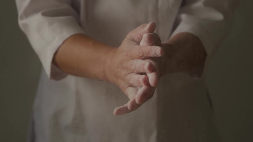 A chef rubs flour on his arms and claps causing the flour to fall off