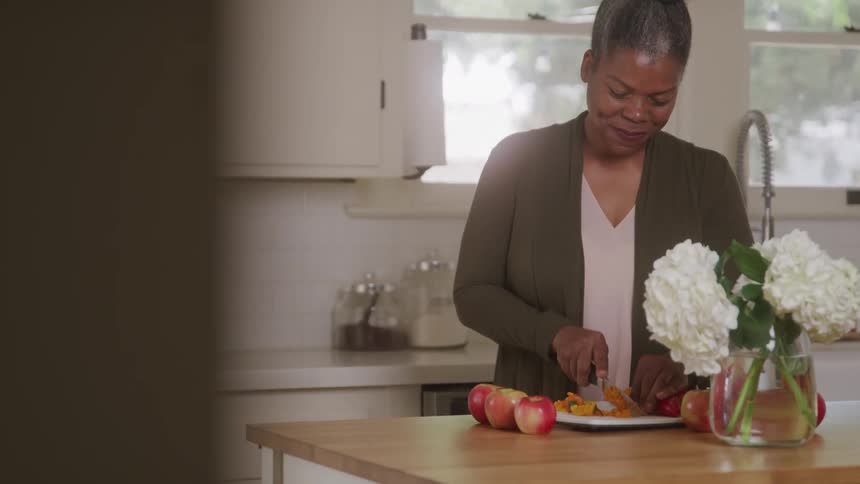 A young black woman chops fruits in a plate on a kitchen counter during daytime