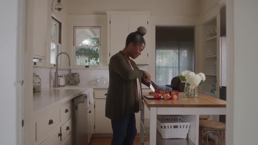 A woman is chopping apples indoor there are some flowers the furniture are looking very modern