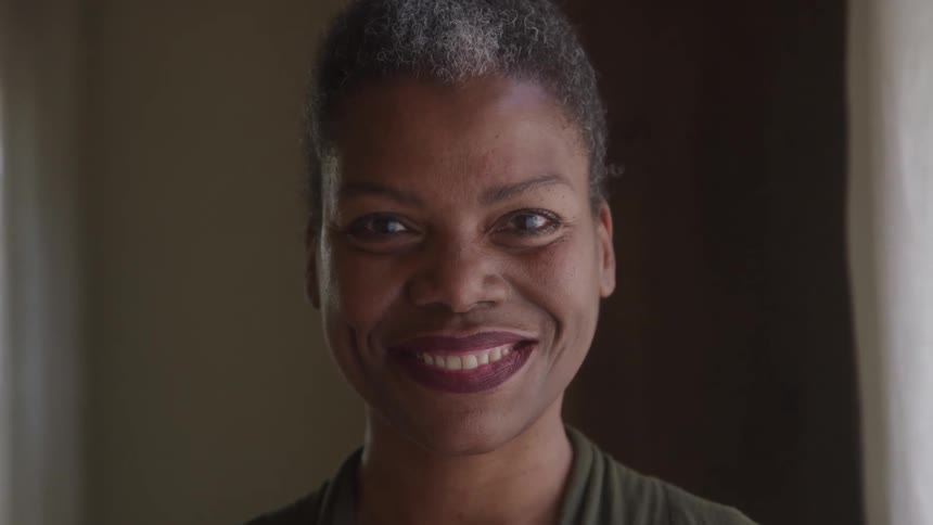 A woman smiles warmly while standing indoors in natural light