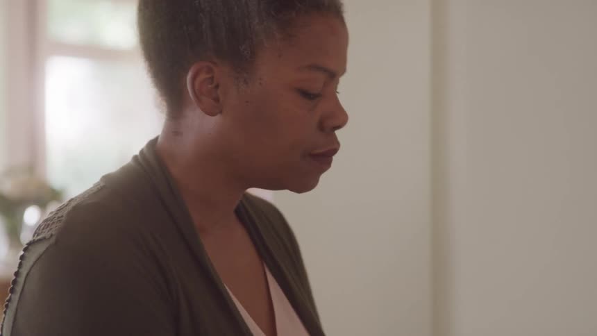 An older adult woman with short grey hair looks down with a contemplative expression seemingly playing piano seen in profile wearing a white top and a green cardigan
