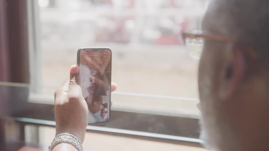 A man holds up his phone during a video call smiling as he chats with a woman on the screen