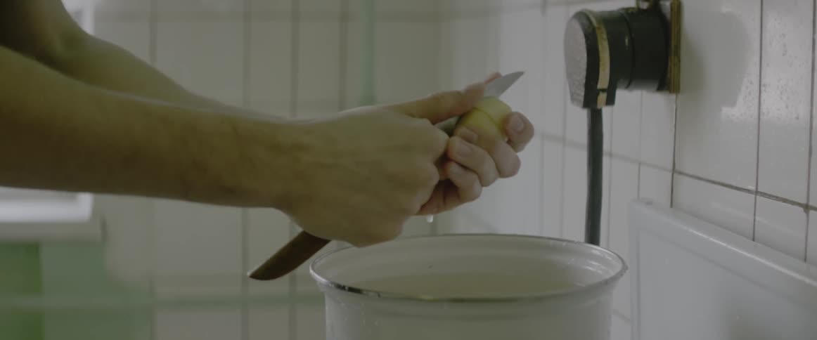 A man is using a knife to cut potatoes in a kitchen