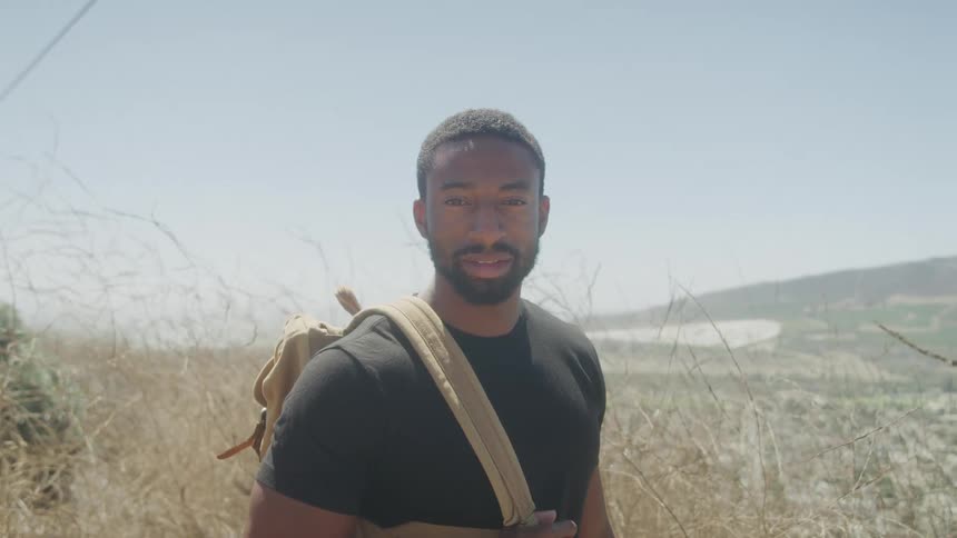 A smiling man with a backpack looks toward the camera