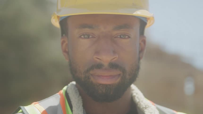 Close up outdoor portrait male construction worker in safety helmet and vest on construction site
