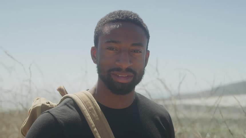 Man with backpack smiles in coastal setting