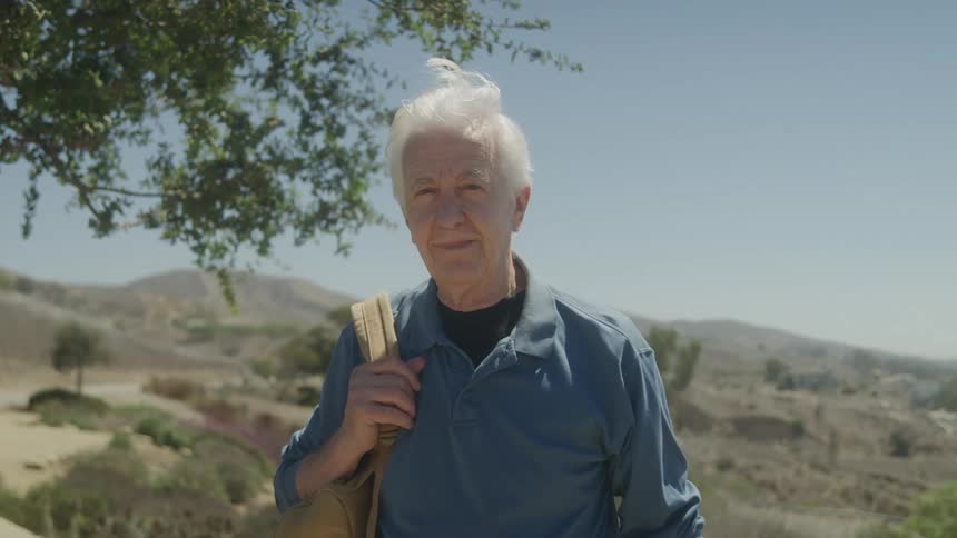 Elderly man in an outdoor setting with mountains in the background