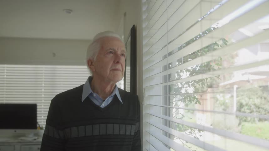 Close up of an elderly man leaning and looking out the window contemplatively in an office area during daytime