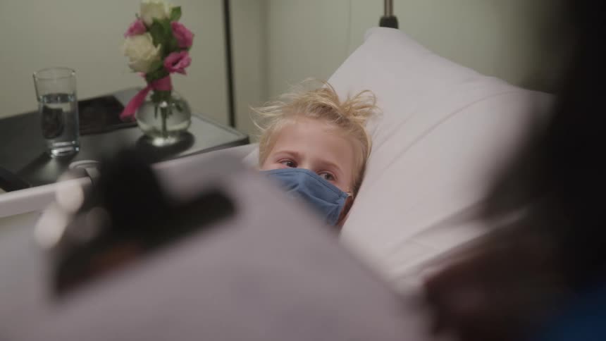 Nurse talking to a little girl lying in a hospital bed