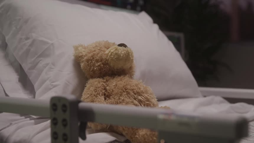 A teddy bear sits on a hospital bed under soft lighting